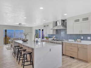 Kitchen with white cabinetry, wall chimney range hood, light hardwood / wood-style floors, a kitchen island with sink, and high end stainless steel range