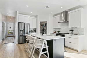 Kitchen with sink, wall chimney exhaust hood, stainless steel appliances, a kitchen island with sink, and white cabinets