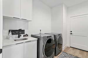 Laundry area with independent washer and dryer, sink, cabinets, and light hardwood / wood-style flooring