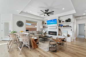 Living room with a raised ceiling, ceiling fan, and light wood-type flooring