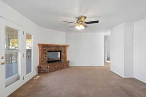 Unfurnished living room featuring ceiling fan, light colored carpet, and a fireplace