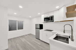 Kitchen with white cabinets, light wood-type flooring, stainless steel appliances, and sink