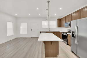 Kitchen with pendant lighting, sink, light hardwood / wood-style floors, a kitchen island, and stainless steel appliances