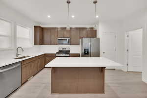 Kitchen featuring sink, a center island, hanging light fixtures, appliances with stainless steel finishes, and light wood-type flooring