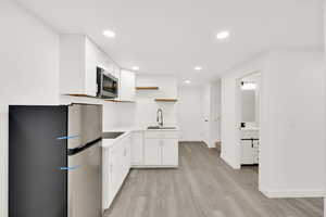 Kitchen featuring stainless steel appliances, white cabinetry, light hardwood / wood-style floors, and sink