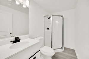 Bathroom featuring hardwood / wood-style floors, vanity, toilet, and a shower with door