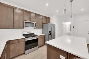 Kitchen featuring dark brown cabinetry, stainless steel appliances, backsplash, pendant lighting, and light wood-type flooring