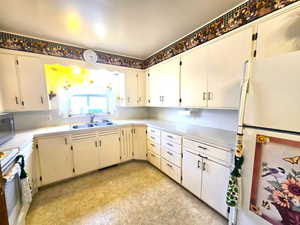 Kitchen with white refrigerator, stove, white cabinetry, and sink