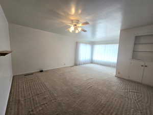 Carpeted spare room featuring built in shelves and ceiling fan