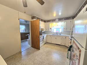 Kitchen with white cabinetry, sink, ceiling fan, and white refrigerator