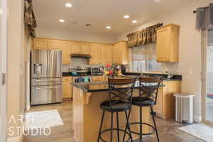 Kitchen with light brown cabinets, a granite center island, stainless steel appliances, sink, and a breakfast bar