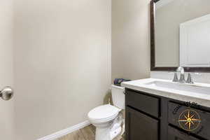 1/2 Bathroom with vanity, toilet, and wood-type flooring