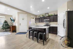 Kitchen featuring a kitchen bar, appliances with stainless steel finishes, light wood-type flooring, sink, and an island with sink