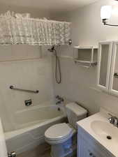 Full bathroom with tiled shower / bath combo, toilet, vanity, tile walls, and wood-style flooring