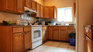 Kitchen featuring white electric range oven, light tile patterned floors, and sink