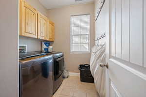 Washroom featuring cabinets, light tile patterned floors, and washer and clothes dryer