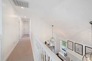 Corridor with light colored carpet, vaulted ceiling, and a notable chandelier