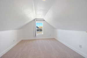 Bonus room with a textured ceiling, light colored carpet, and vaulted ceiling