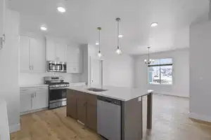 Kitchen with white cabinetry, hanging light fixtures, stainless steel appliances, light hardwood / wood-style floors, and a center island with sink