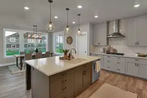 Kitchen with light wood-type flooring, stainless steel appliances, sink, wall chimney range hood, and decorative light fixtures