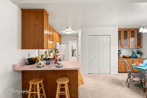 Kitchen featuring white appliances, a textured ceiling, light colored carpet, kitchen peninsula, and a breakfast bar area