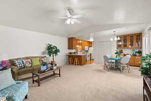 Carpeted living room with a textured ceiling, ceiling fan with notable chandelier, and lofted ceiling