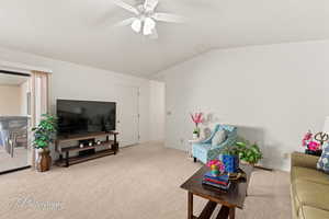 Living room featuring ceiling fan, carpet, and lofted ceiling