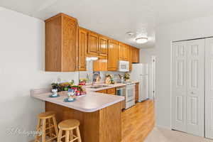 Kitchen featuring sink, a textured ceiling, white appliances, a breakfast bar area, and light wood-type flooring