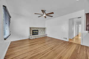 Unfurnished living room featuring ceiling fan, light hardwood floors, and a stone fireplace