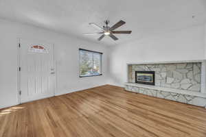 Unfurnished living room with light hardwood  floors, a stone fireplace, and ceiling fan