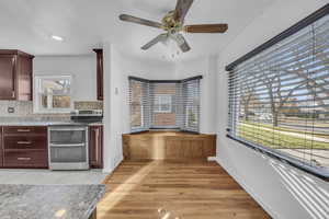 Kitchen with ceiling fan, stainless steel electric stove, decorative backsplash, and bench seat plus hardwood flooring