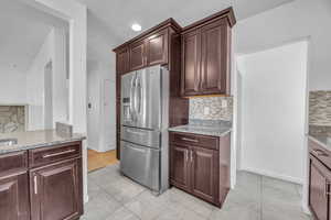 Kitchen featuring decorative backsplash, stainless steel fridge with ice dispenser, and light stone countertops