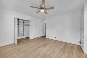 Unfurnished bedroom featuring ceiling fan, hardwood flooring, and an organized closet