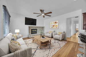 Living room featuring ceiling fan, light hardwood  floors, and a stone fireplace-digitally staged