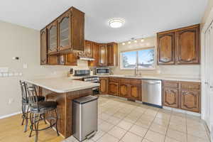 Kitchen featuring light tile patterned floors, kitchen peninsula, sink, and appliances with stainless steel finishes