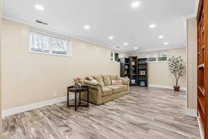 Living room with light hardwood / wood-style floors, ornamental molding, and wood walls