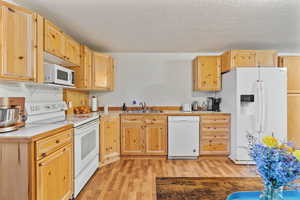 Kitchen with light brown cabinetry, a textured ceiling, white appliances, sink, and light hardwood / wood-style flooring