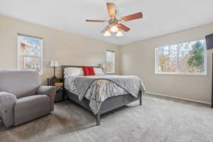 Carpeted bedroom featuring multiple windows and ceiling fan