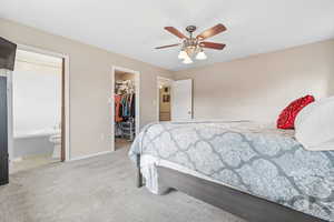 Bedroom with a walk in closet, ensuite bathroom, light colored carpet, ceiling fan, and a closet