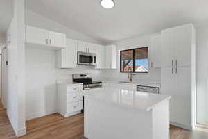 Kitchen with lofted ceiling, white cabinets, sink, a kitchen island, and stainless steel appliances