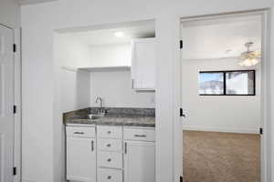 Kitchen with a textured ceiling, ceiling fan, sink, carpet floors, and white cabinetry