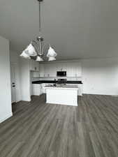 Kitchen featuring appliances with stainless steel finishes, dark hardwood / wood-style flooring, a kitchen island with sink, pendant lighting, and white cabinets