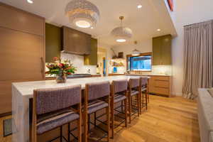 Kitchen with a kitchen breakfast bar, green cabinets, hanging light fixtures, tasteful backsplash, and light hardwood / wood-style floors