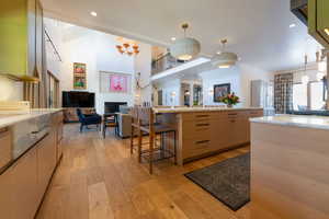 Kitchen with light wood-type flooring, a breakfast bar, light brown cabinets, decorative light fixtures, and a high ceiling