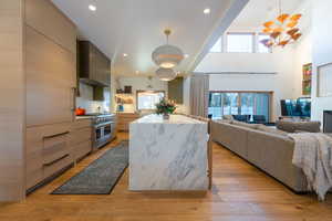 Kitchen with plenty of natural light, range with two ovens, wall chimney range hood, and hanging light fixtures