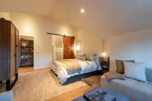 Bedroom with a barn door, light hardwood / wood-style flooring, and lofted ceiling