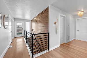 Hall featuring wood walls, light hardwood / wood-style flooring, a chandelier, and a textured ceiling