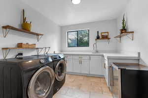 Washroom with washing machine and dryer, sink, light tile patterned floors, and cabinets