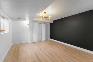 Unfurnished bedroom featuring a textured ceiling, light hardwood / wood-style floors, an inviting chandelier, and a closet