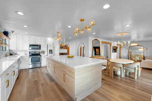 Kitchen with white cabinets, light hardwood / wood-style floors, appliances with stainless steel finishes, and an inviting chandelier